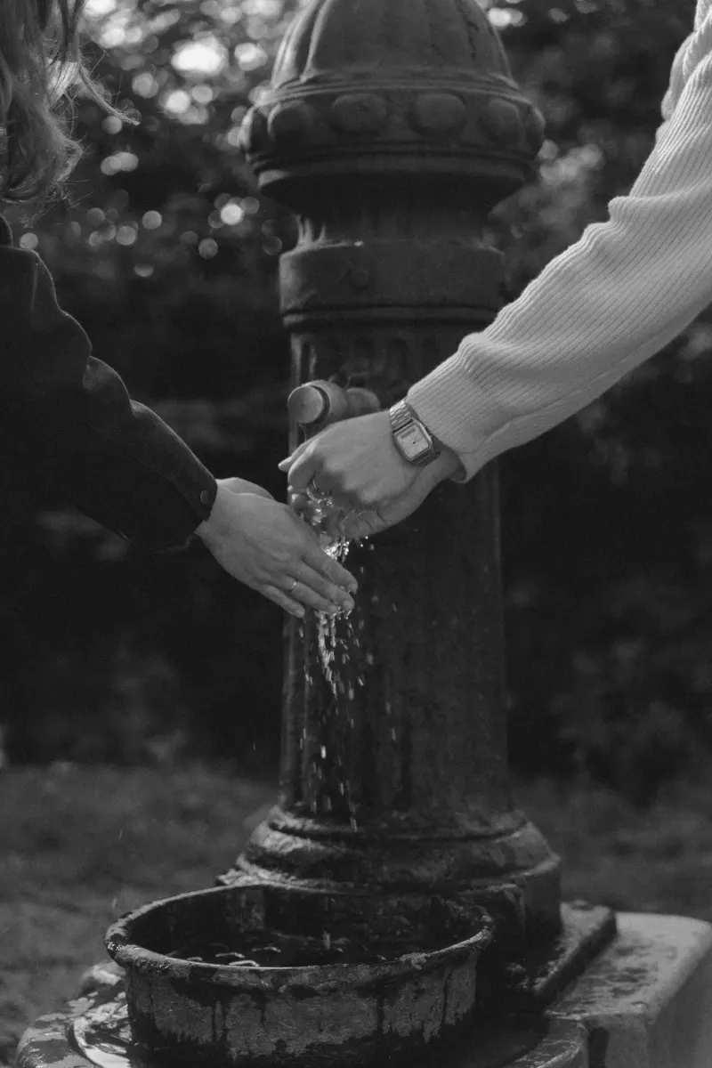 Couple shares a playful moment washing hands together at a vintage fountain during an engagement photoshoot in Barcelona.