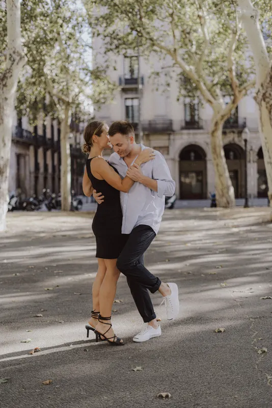 Couple shares a playful, romantic dance beneath city trees during a couples & engagements photoshoot outdoors.