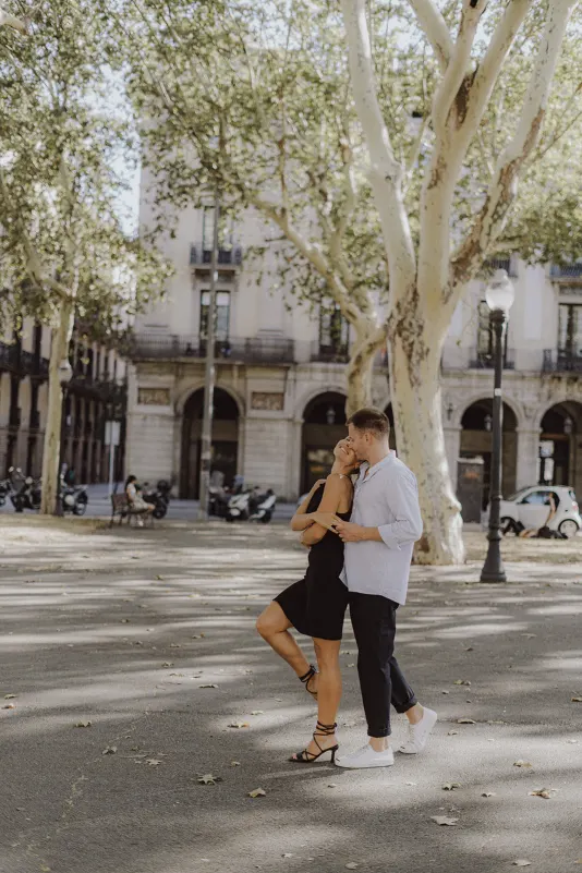 Couple shares a playful, romantic moment under city trees during a couples & engagements photoshoot.