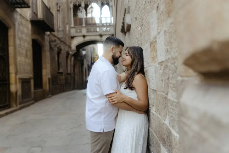 Couple shares a quiet, affectionate moment against a stone wall during their engagement photoshoot in a historic city street.