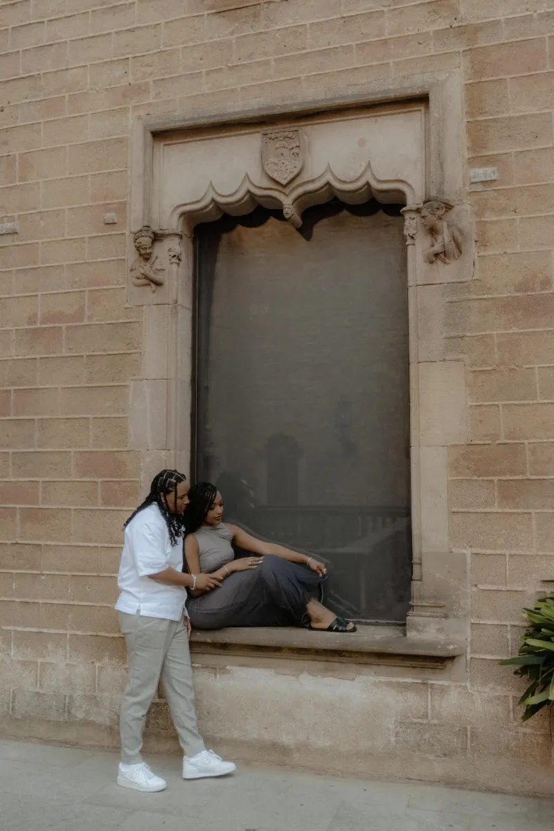 Couple shares a quiet, affectionate moment by a historic window during their surprise proposal photoshoot in Barcelona.