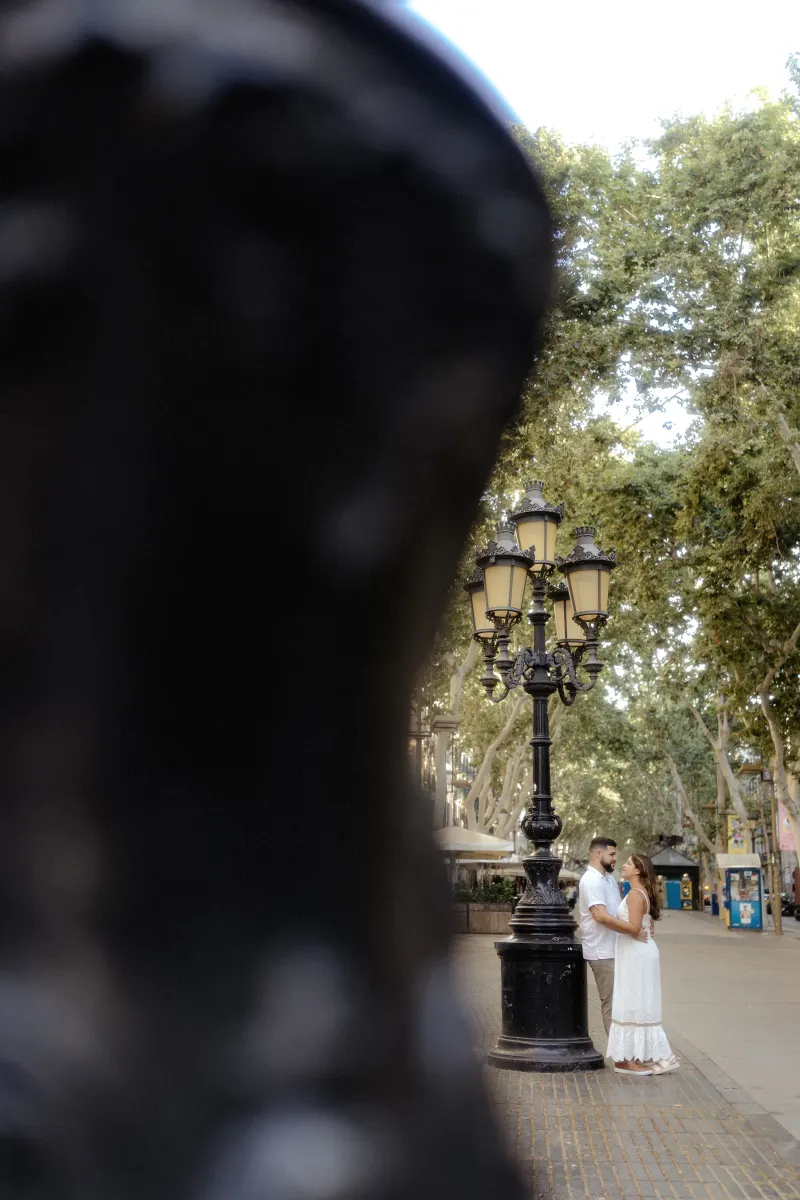 Couple shares a quiet, affectionate moment by a vintage lamppost during their engagement photoshoot in a tree-lined plaza.