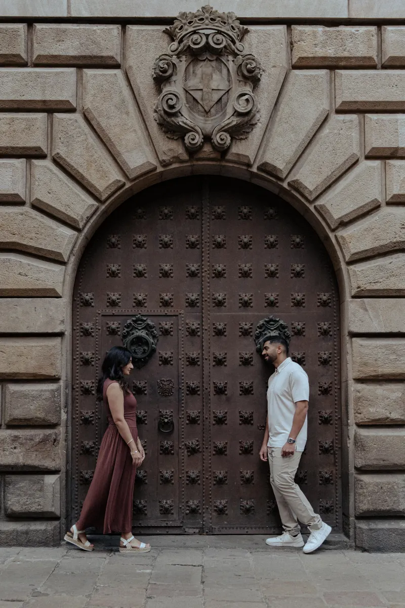 Couple shares a quiet, affectionate moment facing each other by an ornate doorway during their engagement photoshoot.