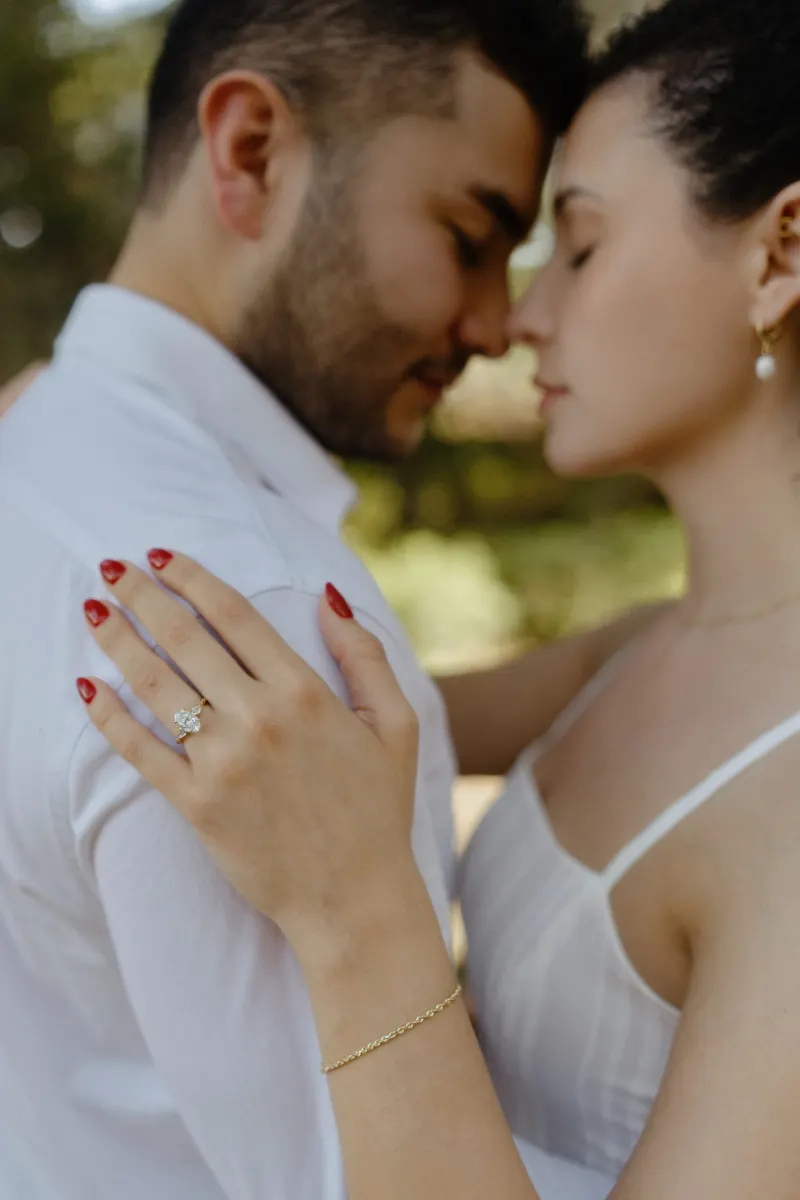Couple shares a quiet embrace, her engagement ring in focus, during a romantic couples & engagements photoshoot outdoors.