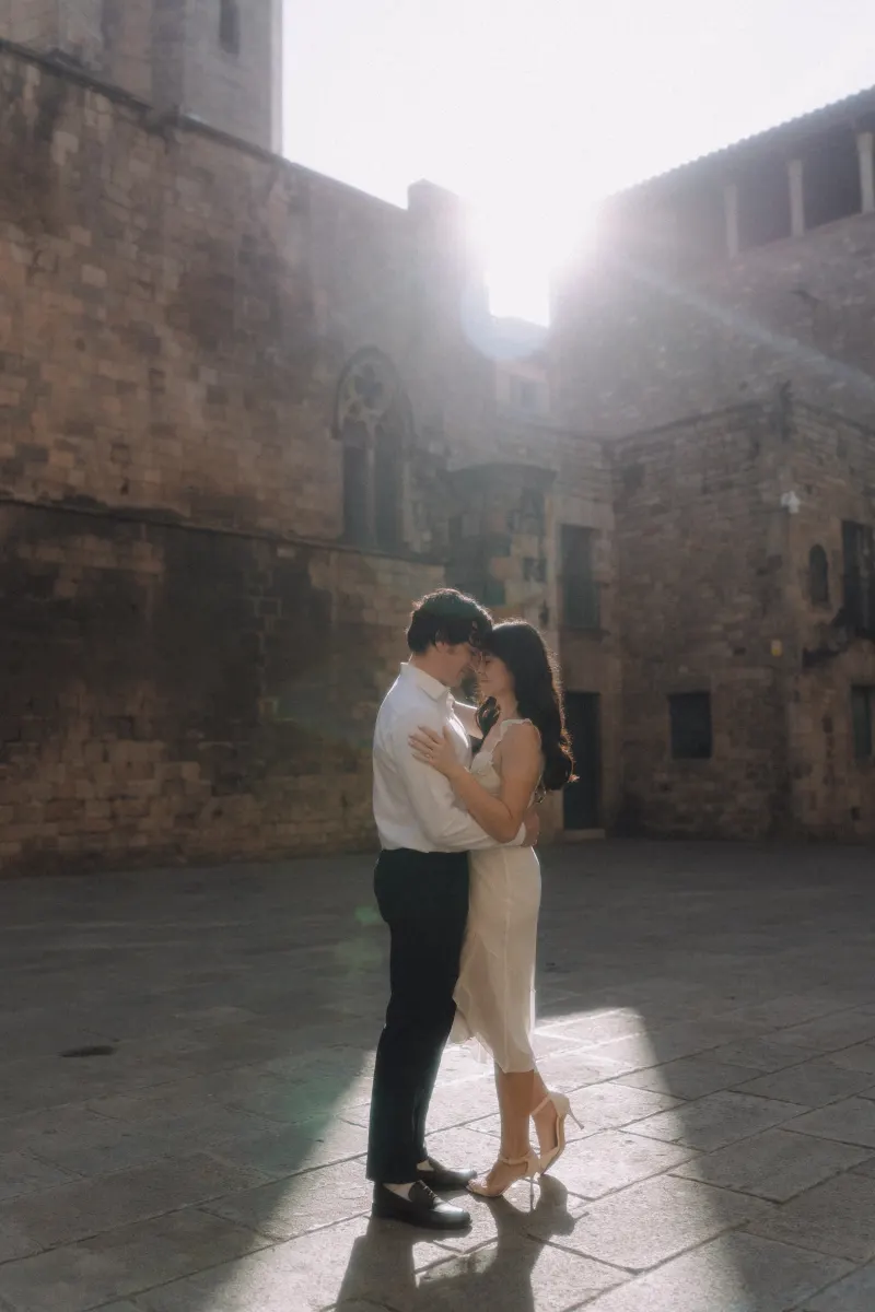 Couple shares a quiet embrace in golden sunlight against historic stone walls during a couples & engagements photoshoot.