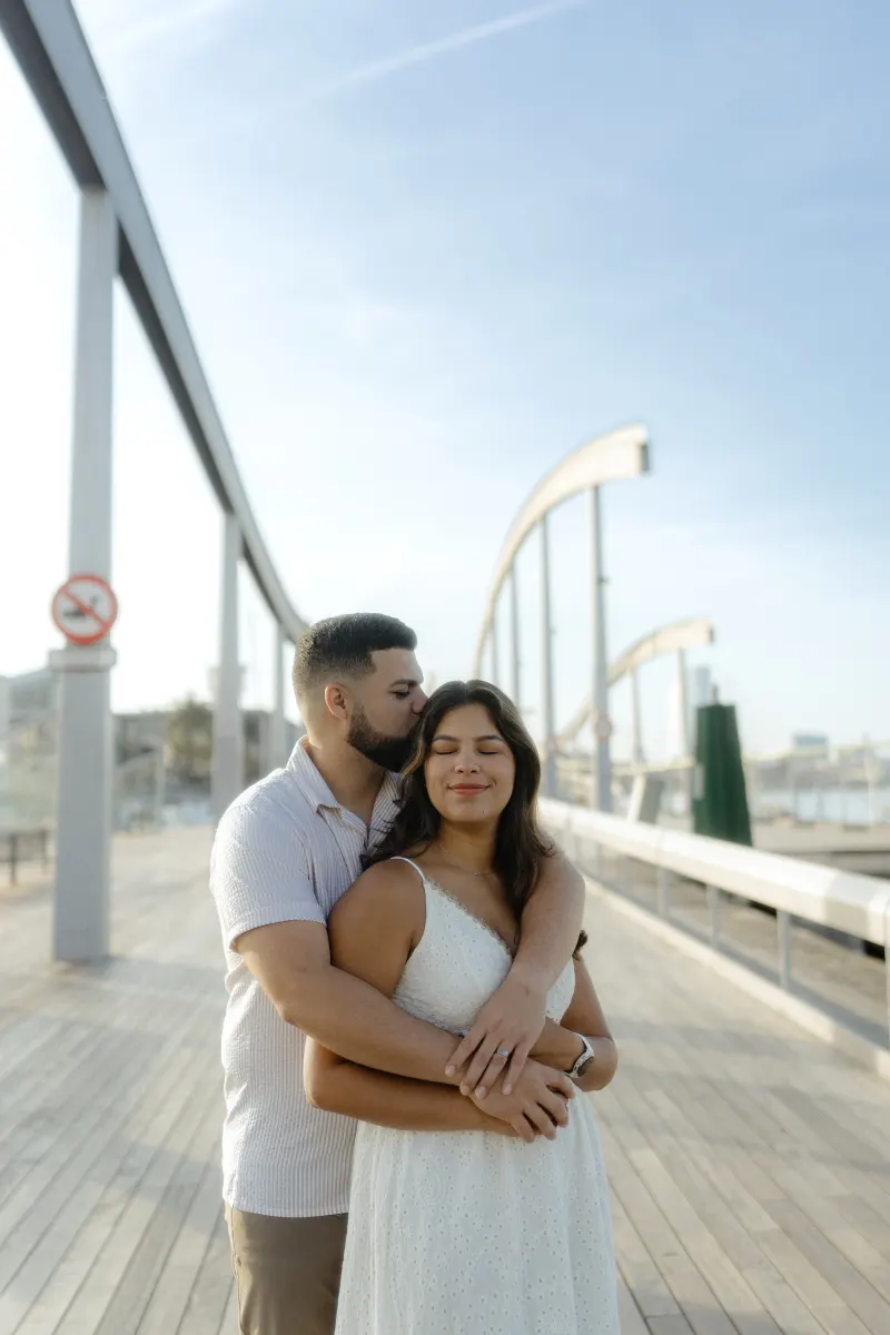 Couple shares a quiet embrace on a sunlit boardwalk, captured during a couples & engagements photoshoot by the marina.