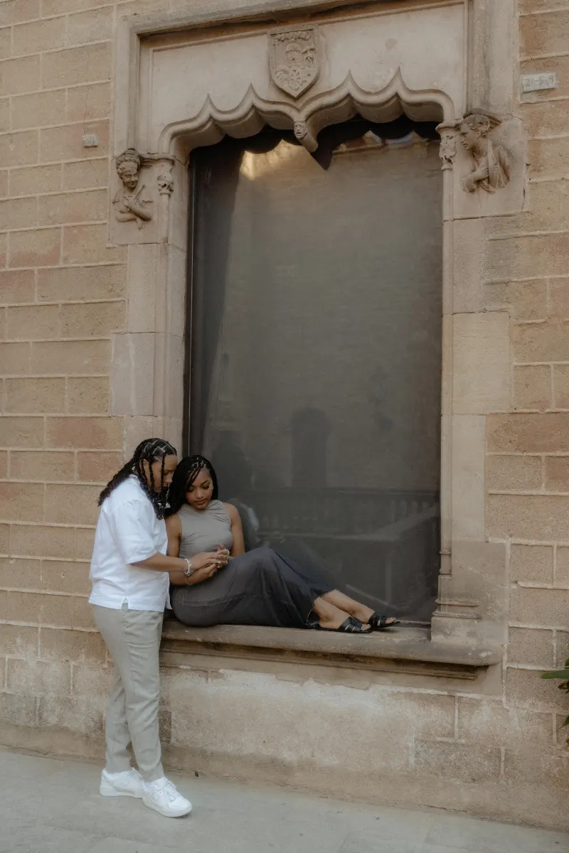Couple shares a quiet, emotional moment by a historic window during their surprise proposal photoshoot in Barcelona.