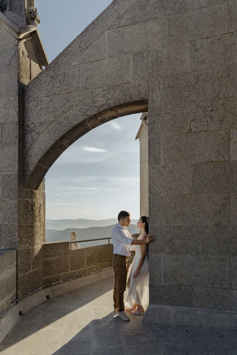 Couple shares a quiet, intimate moment beneath a stone archway during their engagement photoshoot at a historic landmark.