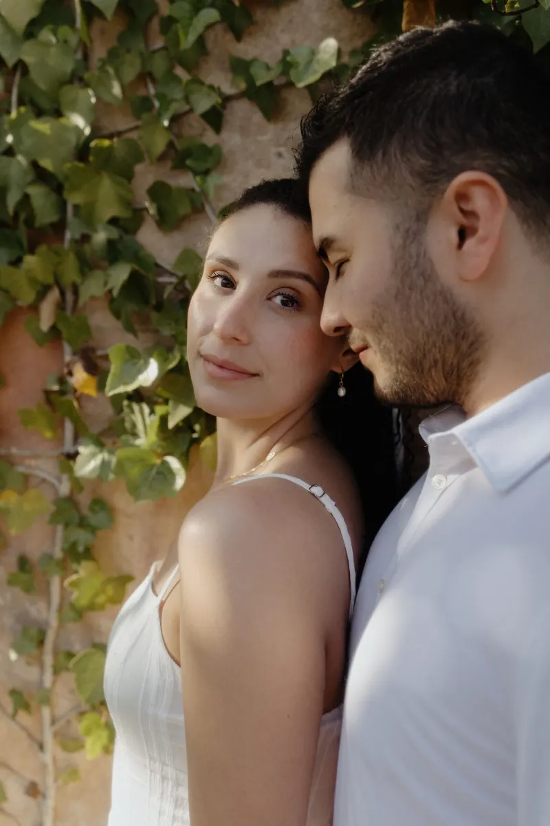 Couple shares a quiet, intimate moment by a sunlit ivy wall during their couples & engagements photoshoot.