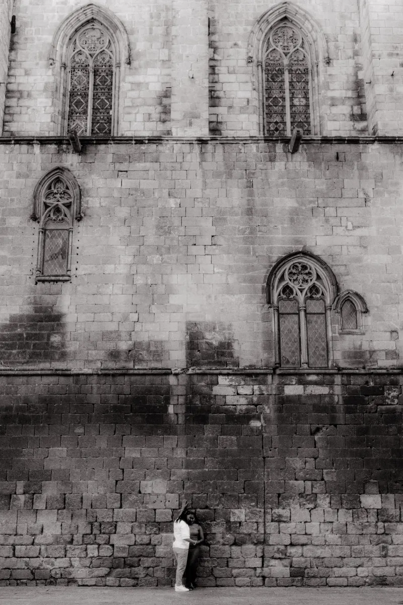 Couple shares a quiet, loving embrace against the historic stone wall during a surprise proposal photoshoot in Barcelona.