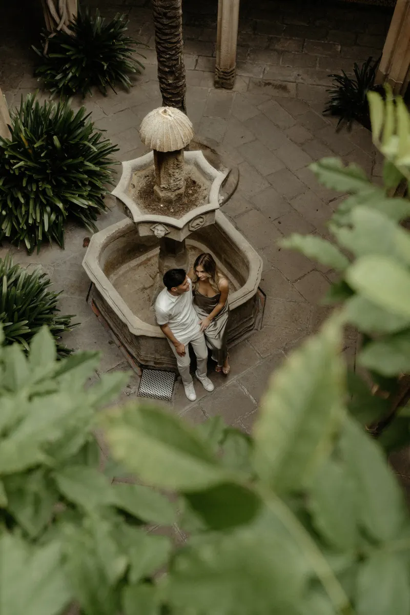 Couple shares a quiet moment by a historic courtyard fountain in Barcelona during their Vacation Portraits photoshoot.