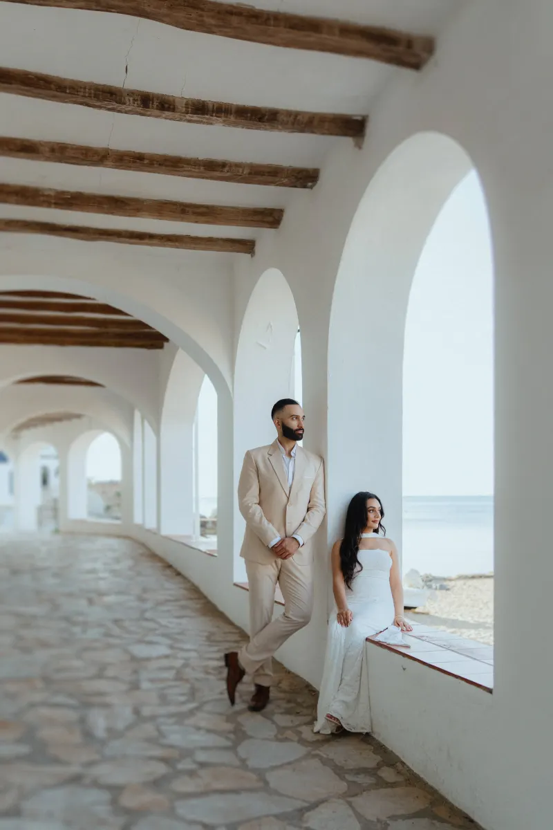 Couple shares a quiet moment by the seaside during a surprise proposal photoshoot in a sunlit Mediterranean corridor.