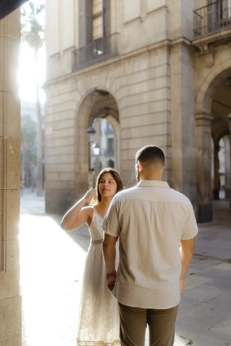 Couple shares a quiet moment in soft sunlight beneath historic arches during a couples & engagements photoshoot.