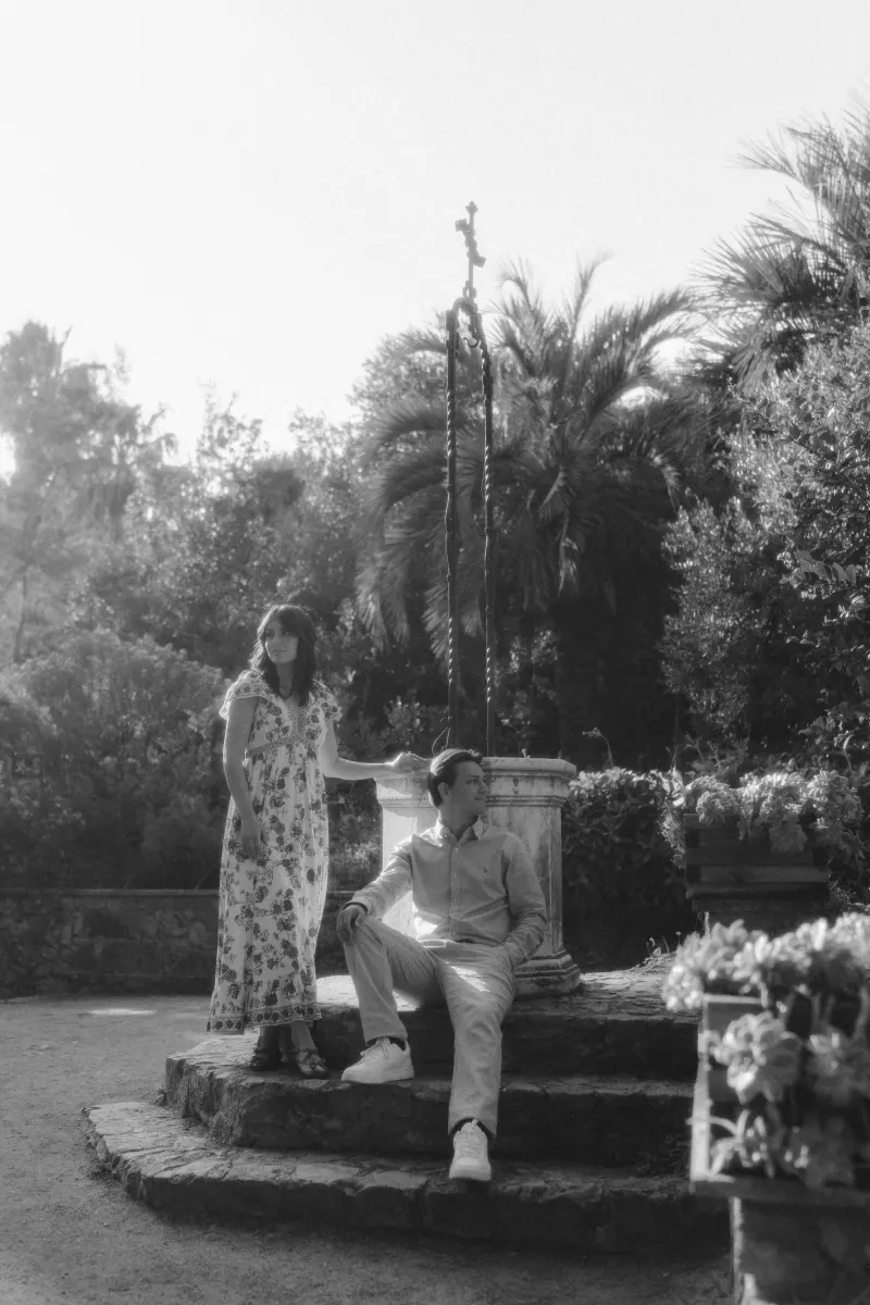 Couple shares a quiet, reflective moment by a Mediterranean garden well during a surprise proposal photoshoot.