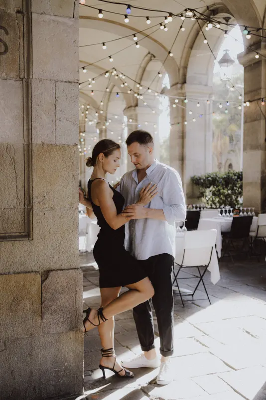 Couple shares a quiet, romantic moment beneath string lights at an elegant outdoor café during an engagement photoshoot.