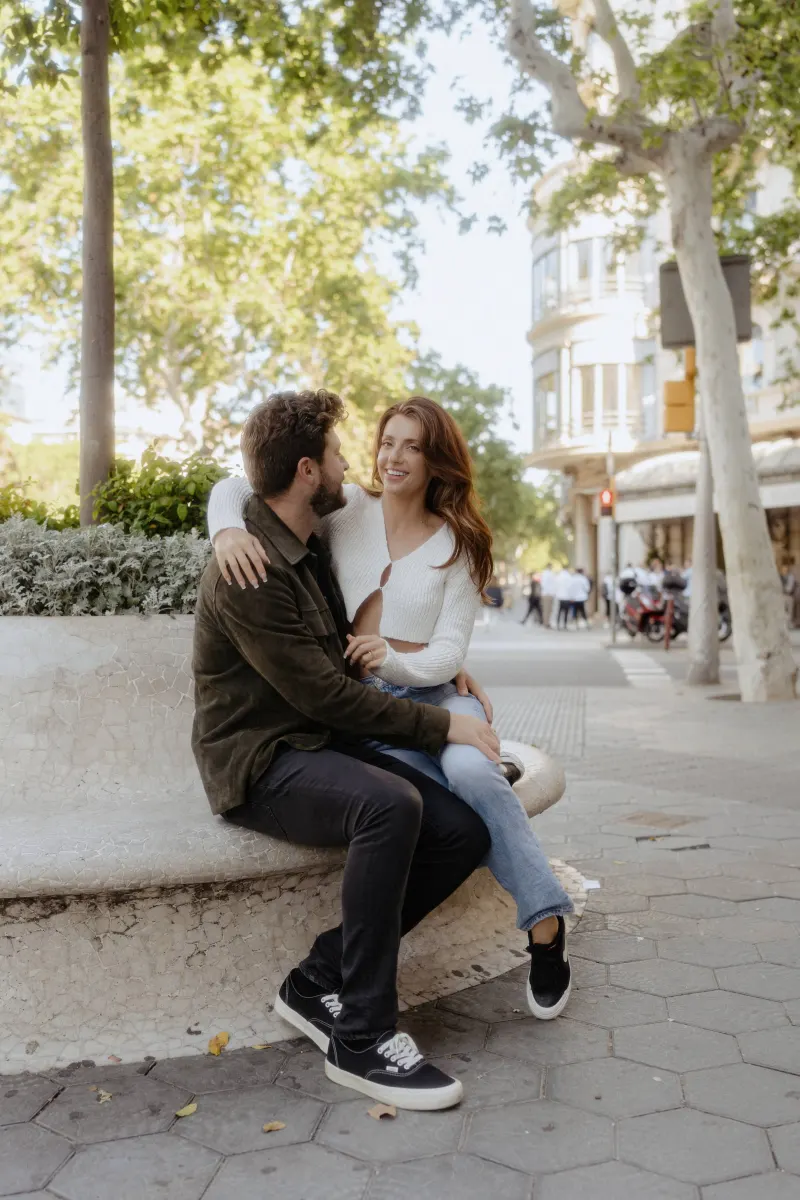 Couple shares a relaxed, affectionate moment on a sunlit city bench during a couples & engagements photoshoot.