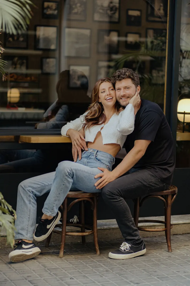 Couple shares a relaxed, joyful moment seated outside a café during a couples & engagements photoshoot in the city.