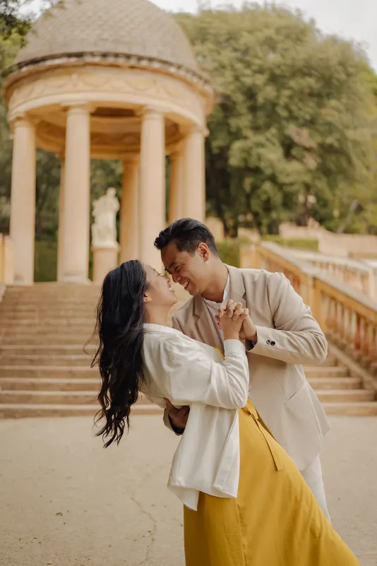 Couple shares a romantic dance and laughter in front of a classical pavilion during a couples & engagements photoshoot.