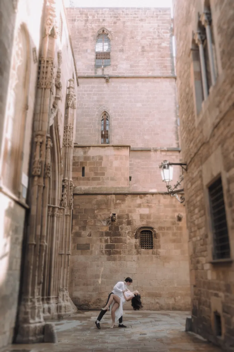 Couple shares a romantic dance dip in a sunlit Gothic Quarter alley during their couples & engagements photoshoot.