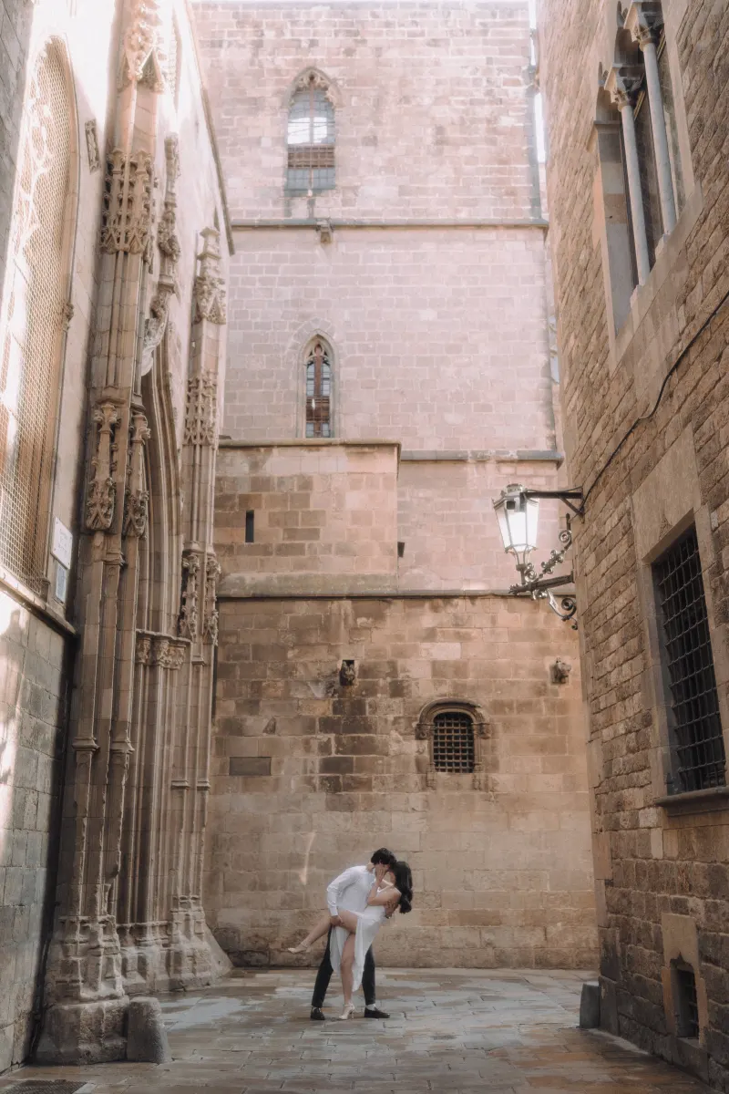 Couple shares a romantic dip and kiss in a sunlit Gothic Quarter alley during their couples & engagements photoshoot.