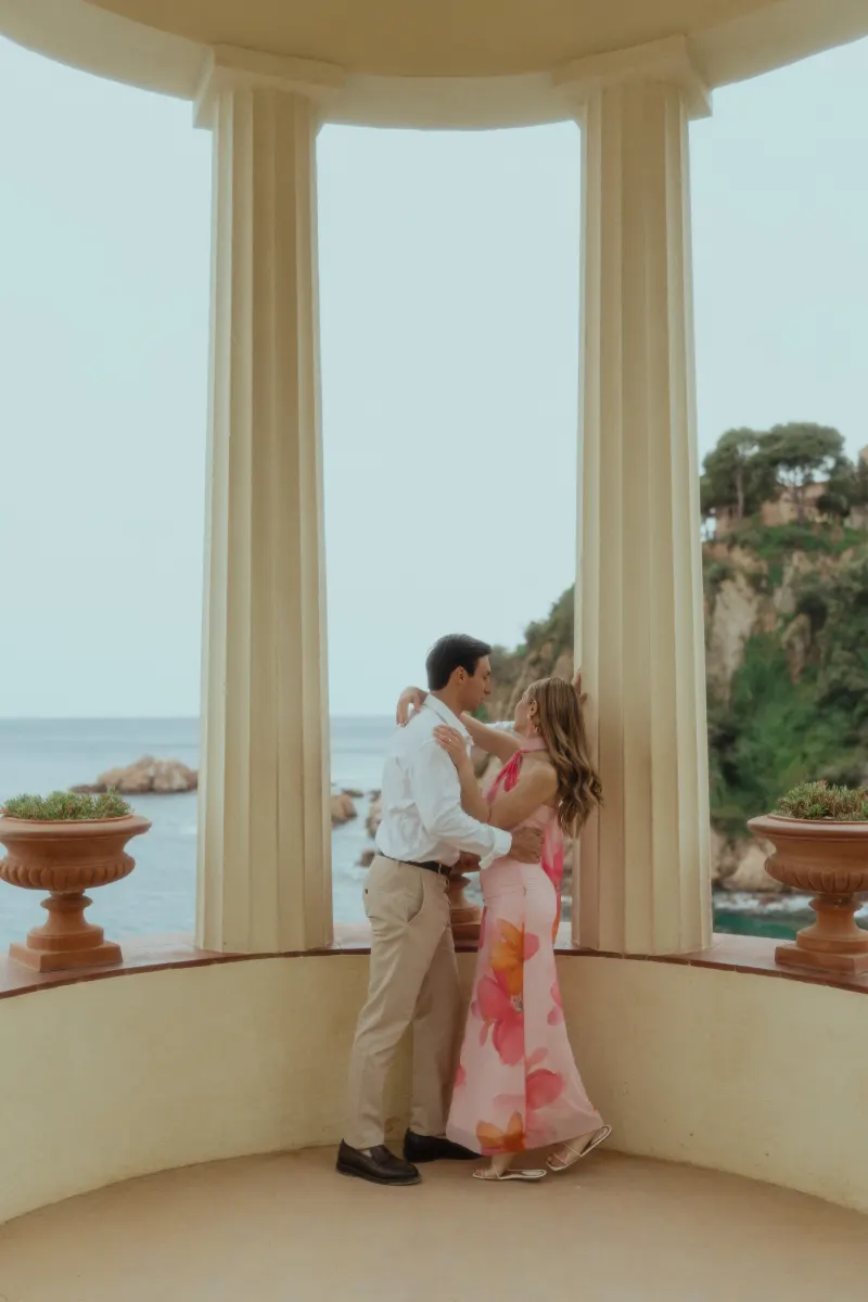 Couple shares a romantic embrace in a seaside pavilion during a surprise proposal photoshoot.