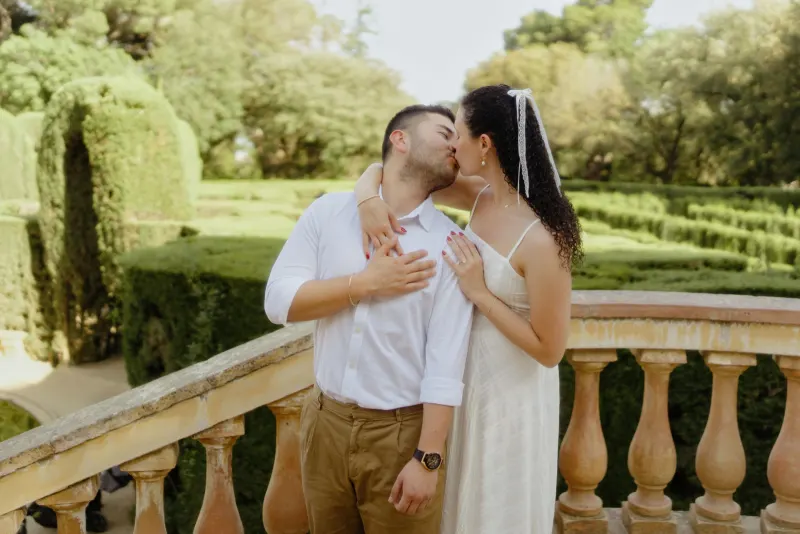 Couple shares a romantic kiss on a sunlit garden terrace during a couples & engagements photoshoot.