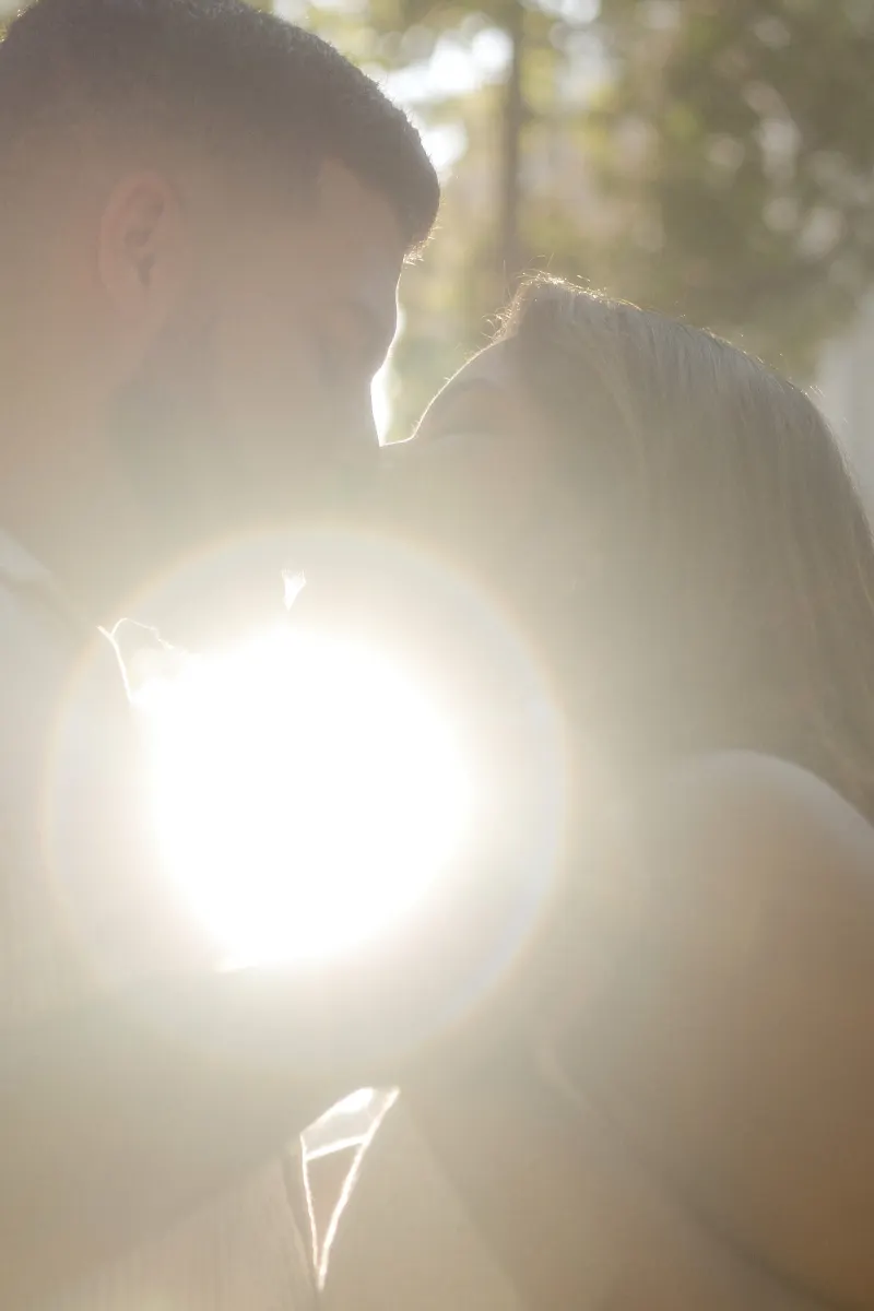 Couple shares a soft kiss in golden sunlight, captured during a romantic couples & engagements photoshoot outdoors.
