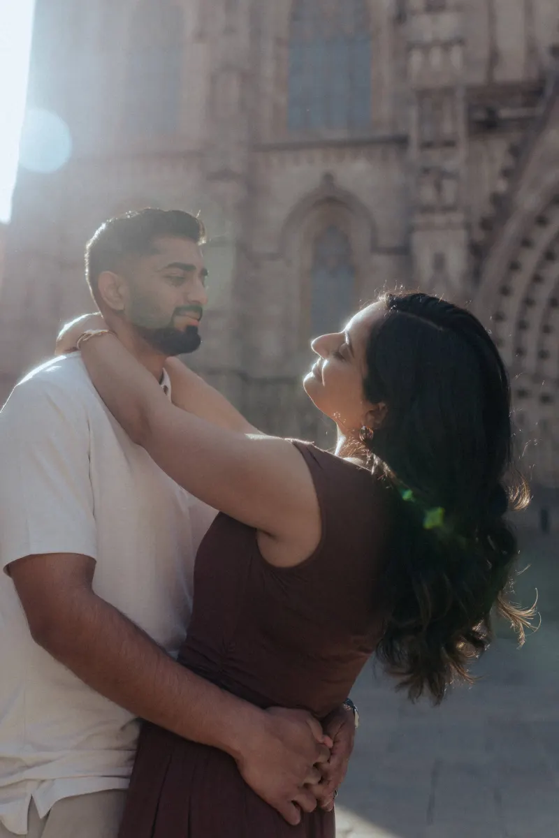 Couple shares a soft, sunlit embrace outside a historic cathedral during their couples & engagements photoshoot.