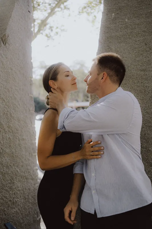 Couple shares a tender, almost-kiss moment between stone pillars during an outdoor couples & engagements photoshoot.