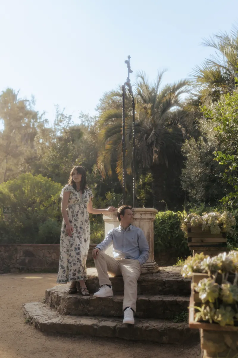 Couple shares a tender moment by a Mediterranean garden well during a surprise proposal photoshoot.