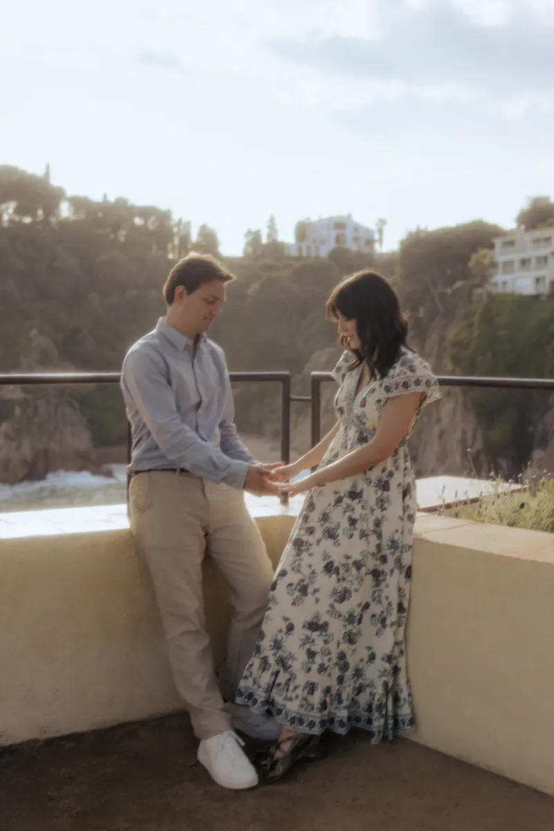 Couple shares a tender moment by the seaside, holding hands after a surprise proposal photoshoot in the Mediterranean.