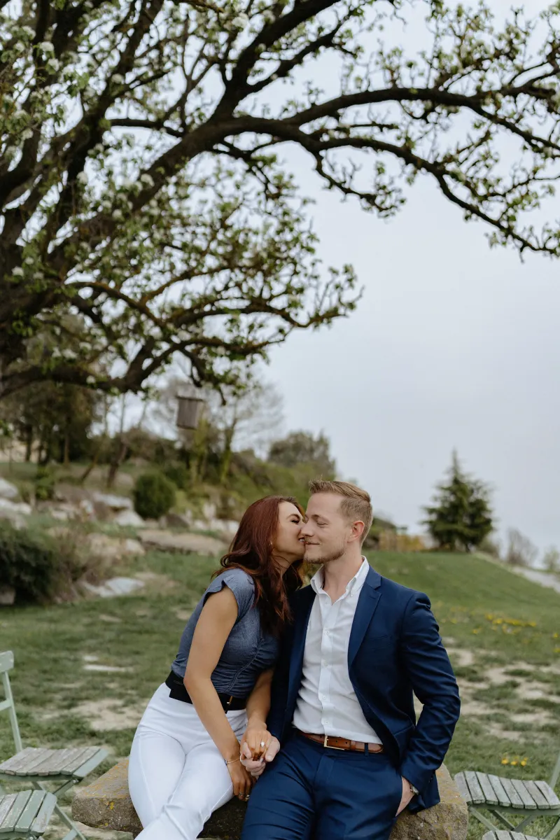 Couple shares a tender moment on a countryside bench, holding hands during their surprise proposal photoshoot.