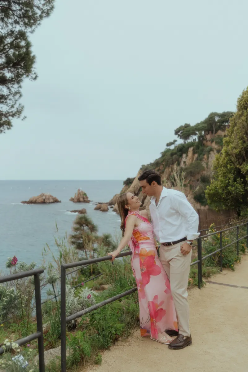 Couple shares a tender moment on a seaside path, captured during a surprise proposal photoshoot on the coast.