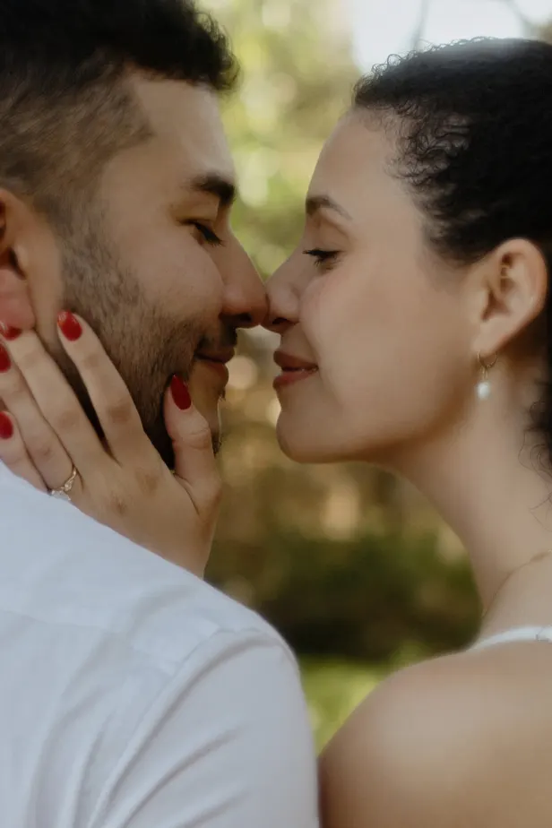 Couple shares a tender, nose-to-nose moment outdoors, her hand on his cheek during a couples & engagements photoshoot.