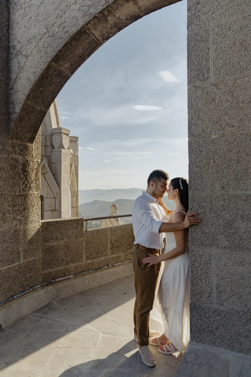 Couple shares a tender, sunlit embrace beneath a stone archway during their engagement photoshoot at a historic landmark.