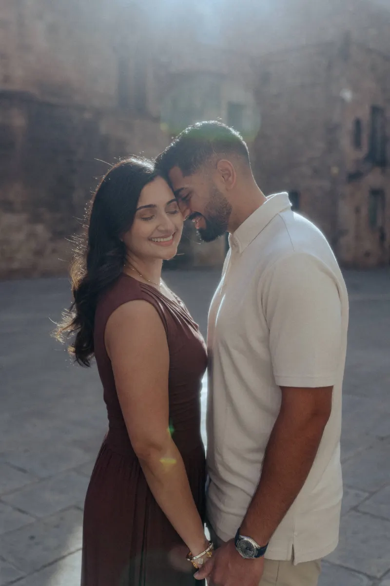 Couple shares a tender, sunlit moment during their engagement photoshoot in a historic European courtyard.
