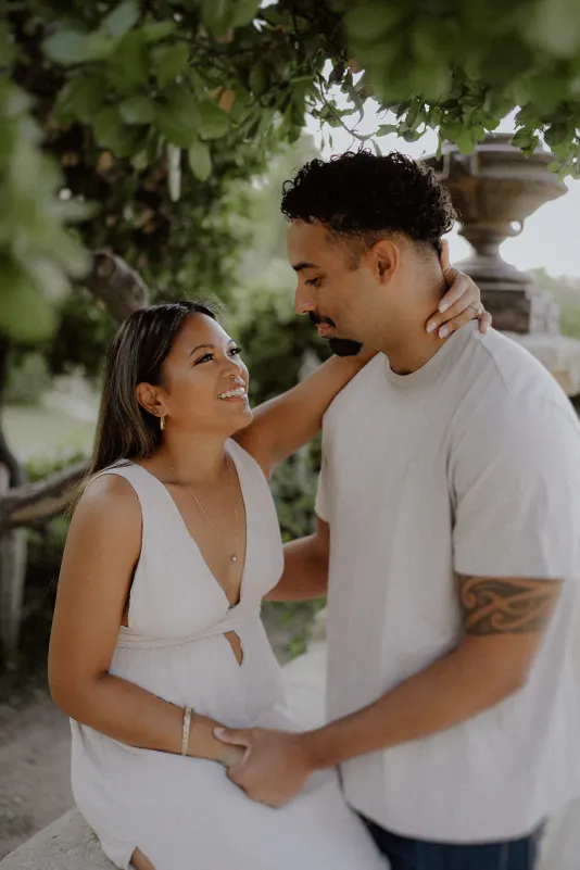 Couple shares a warm, affectionate gaze beneath leafy branches during a romantic engagement photoshoot in the garden.