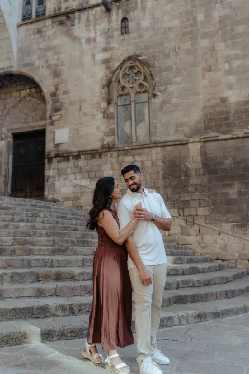 Couple shares a warm, candid moment on stone steps during a couples & engagements photoshoot in a historic city setting.