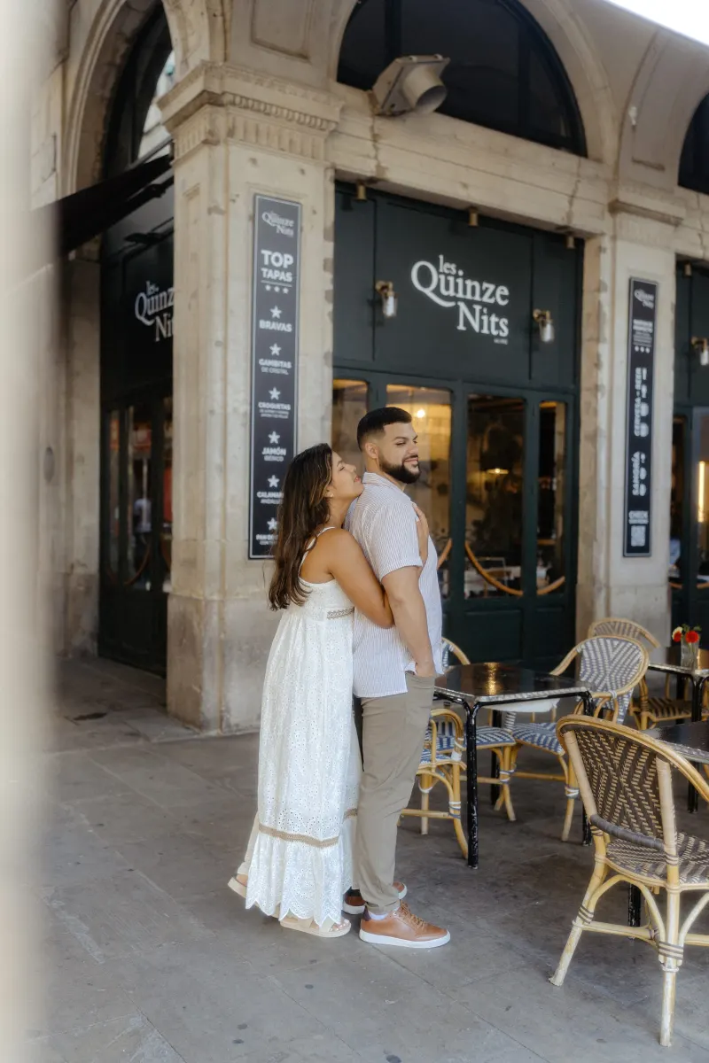 Couple shares a warm embrace outside a charming café during their couples & engagements photoshoot in the city.