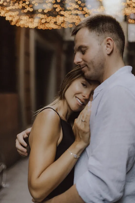 Couple shares a warm embrace under twinkling lights, capturing a tender moment during a couples & engagements photoshoot.