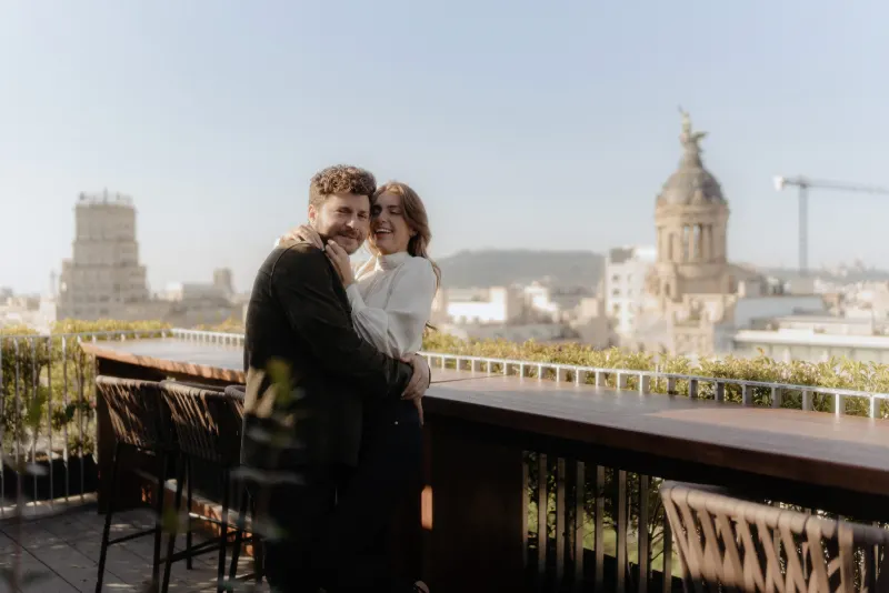 Couple shares a warm hug and laughter on a sunlit rooftop, captured during a couples & engagements photoshoot.