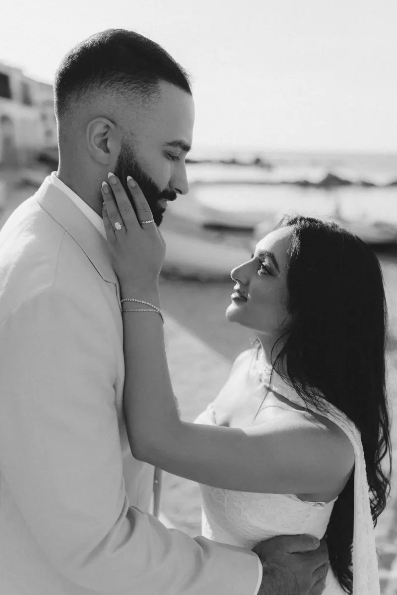 Couple shares an emotional moment on the beach after a surprise proposal photoshoot, her ring sparkling in the sunlight.