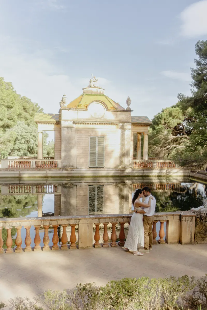Couple shares an intimate embrace by a reflective pond and classical pavilion during a couples & engagements photoshoot.