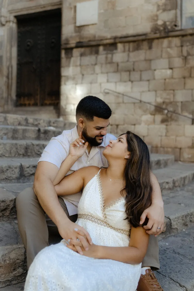 Couple shares an intimate, joyful moment seated on historic stone steps during an engagement photoshoot in the old city.