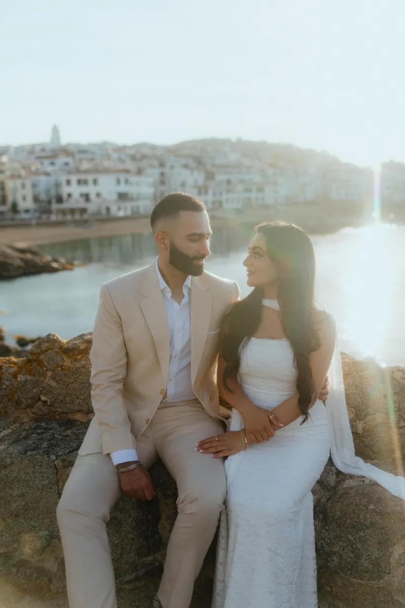 Couple shares an intimate moment by the water at sunset during a surprise proposal photoshoot in a coastal town.