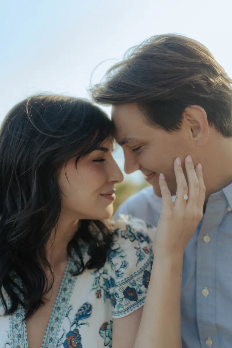 Couple shares an intimate moment, her engagement ring sparkling, during a surprise proposal photoshoot outdoors.