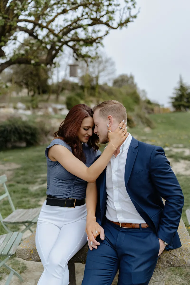 Couple shares an intimate moment on a countryside bench, celebrating their engagement during a surprise proposal photoshoot.