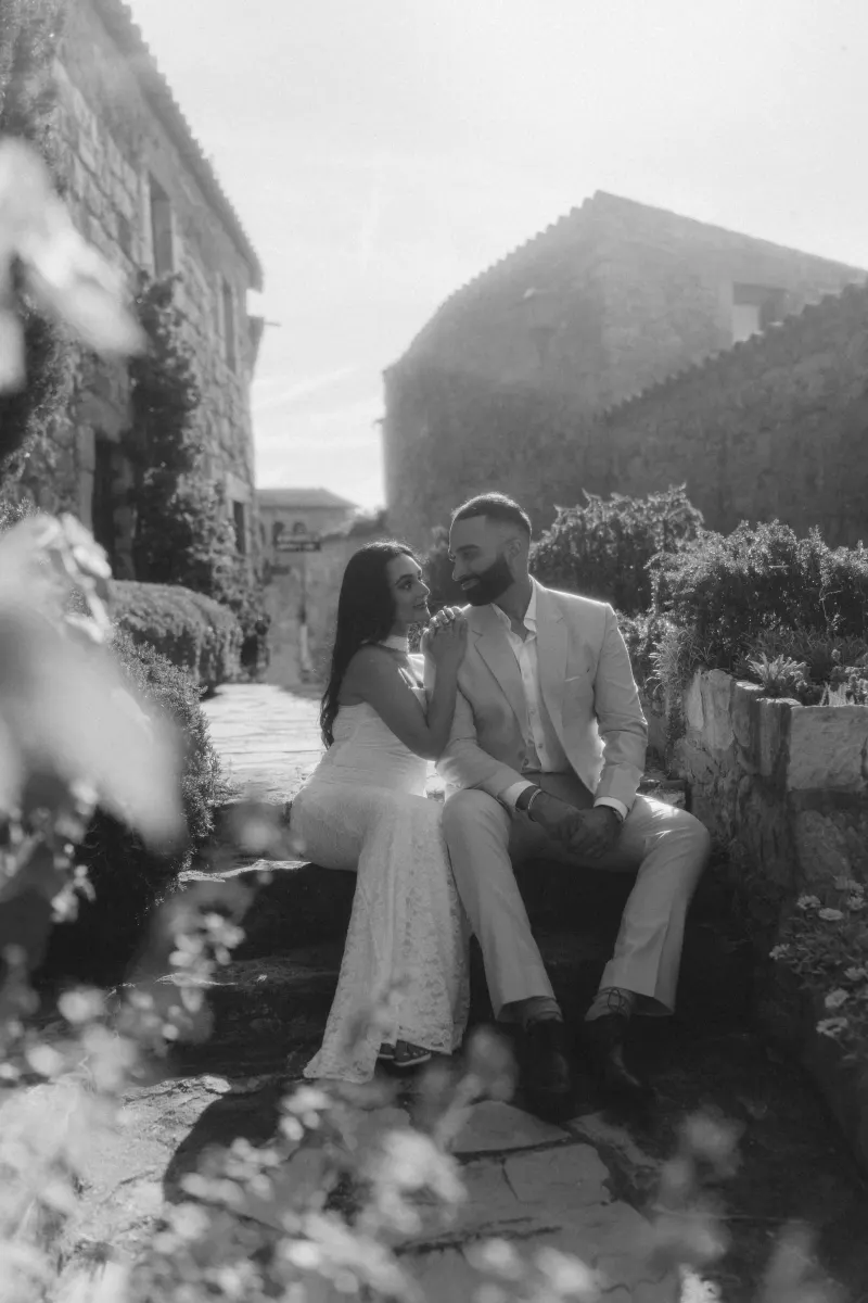 Couple shares an intimate moment on stone steps in a sunlit village, captured during a surprise proposal photoshoot.