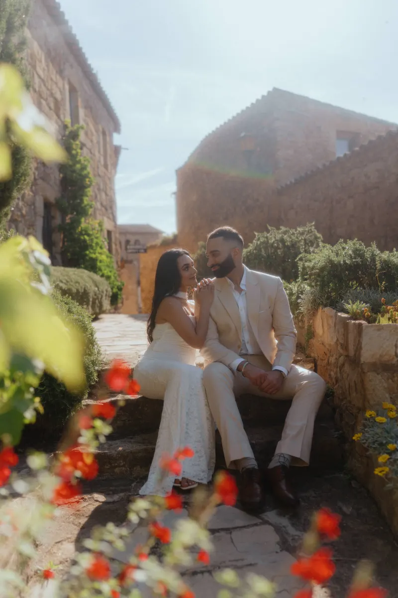 Couple shares an intimate moment on stone steps in a sunlit village, captured during their surprise proposal photoshoot.