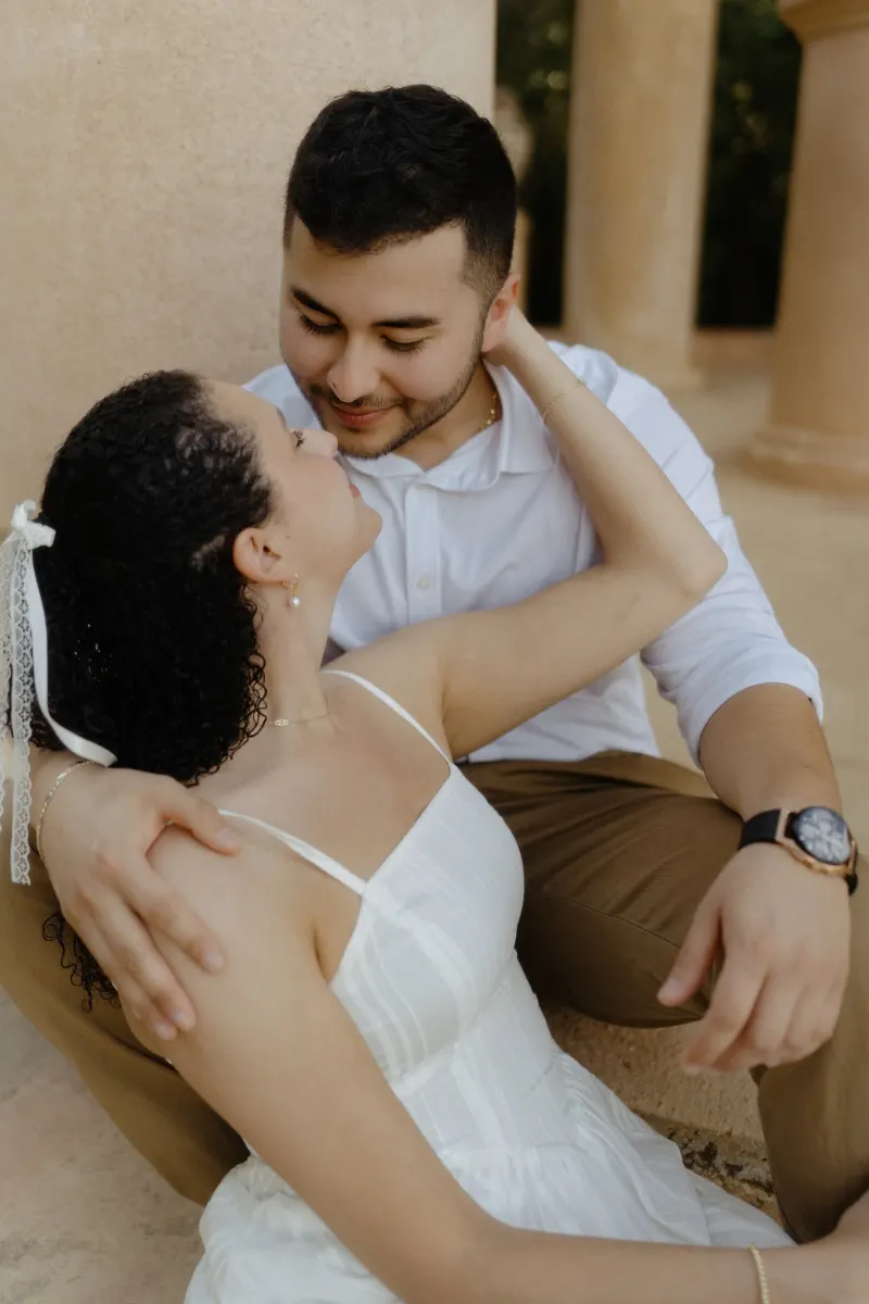Couple shares an intimate moment on stone steps, smiling softly during a couples & engagements photoshoot at a pavilion.